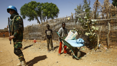 Sudanese boys push a wheelbarrow past a United Nations peace keeper at the El-Riyadh camp for internally displaced persons in el-Geneina, on February 8, 2017
