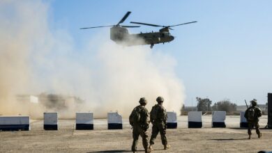 American troops walk as a US Army C-47 Chinook helicopter flies over the village of Oreij, south of Mosul, Iraq