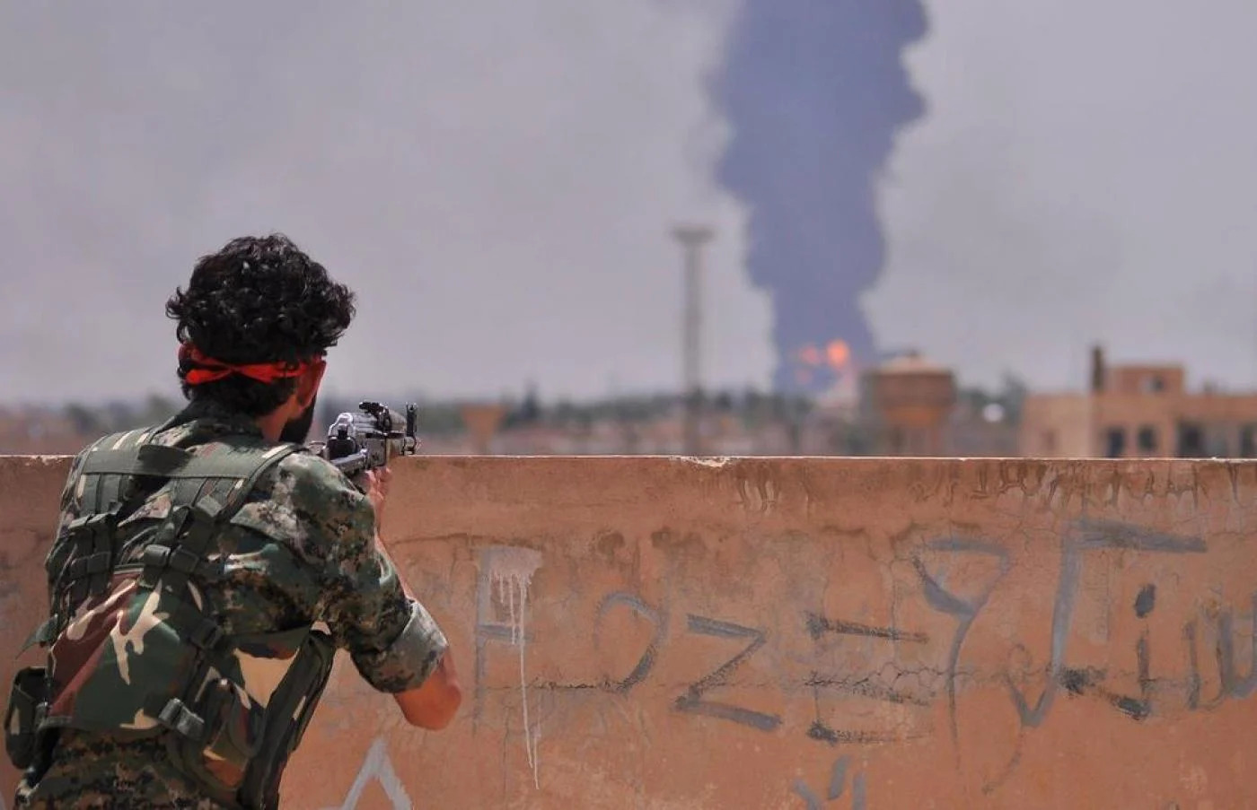 A Kurdish fighter with the People's Protection Units (YPG) looks on at an air strike in the distance