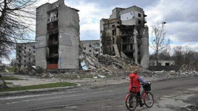 A woman carries her bicycle past destroyed buildings in the town of Borodianka, northwest of Kyiv