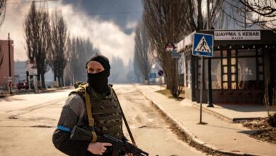 A Ukrainian serviceman stands guard near a burning warehouse hit by a Russian shell in the suburbs of Kyiv