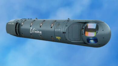 A LITENING 5 Target Pod. The capsule-shaped targetting system is painted gray-green and has "Litening" painted in white in the middle of it.