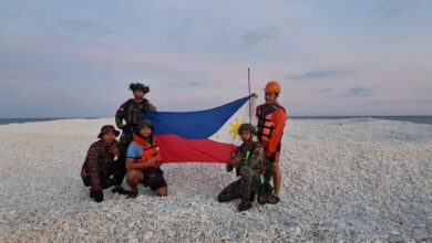 The Philippine Coast Guard holding the country's flag over the disputed Sandy Cay reef in the South China Sea.