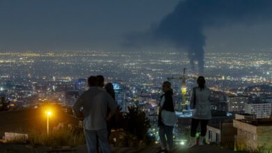 People gather on a hill to watch smoke rising in the distance from an Israeli airstrike in Tehran, Iran, on June 14, 2025