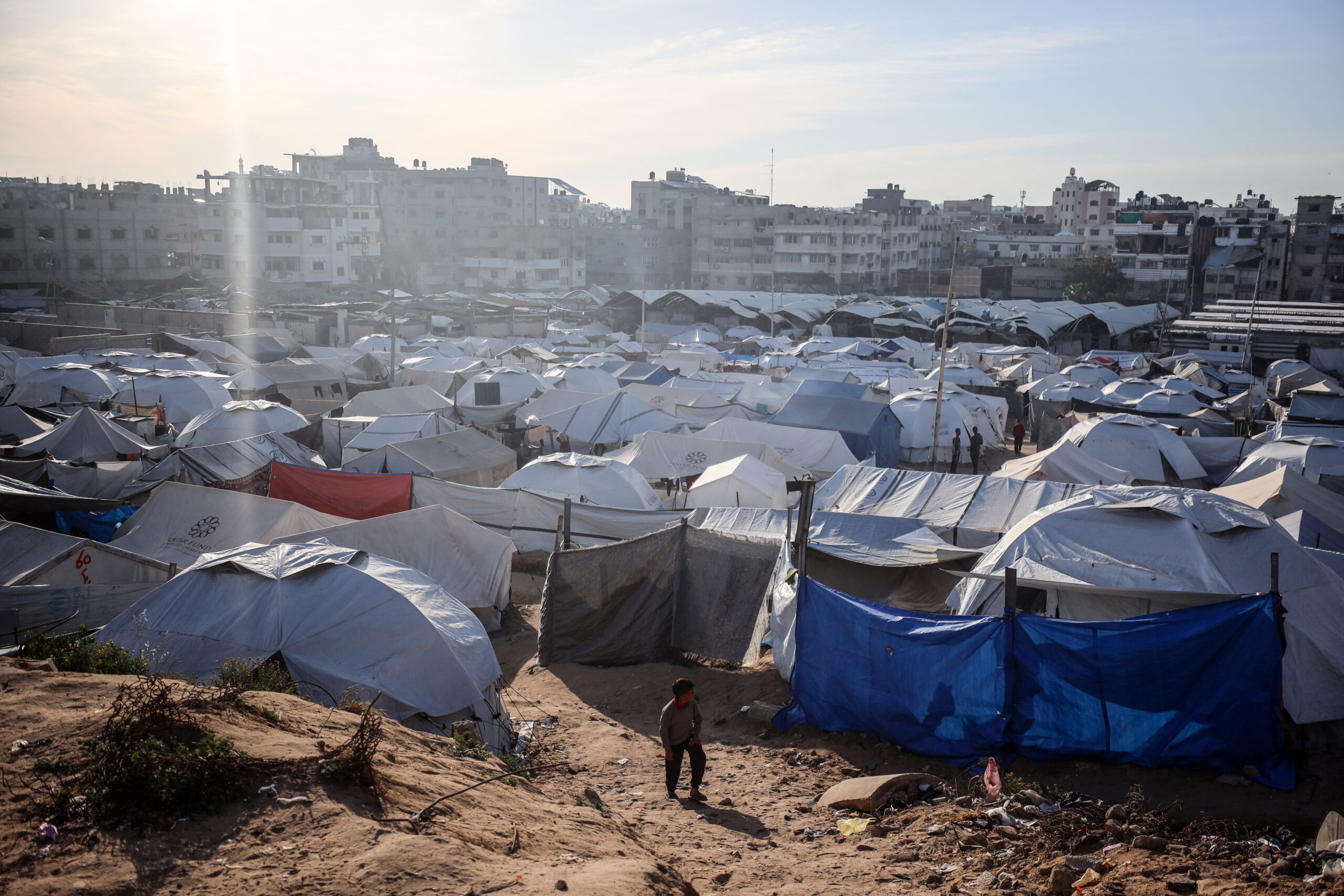palestine-boy-walks-in-front-of-white-tents-gaza