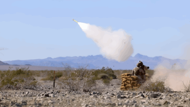A soldier firing a missile in a sandy environtment with a clear daylight background