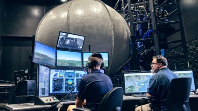 Two people in a control room operate flight simulators with multiple screens displaying maps and cockpit views, creating a focused and high-tech environment.