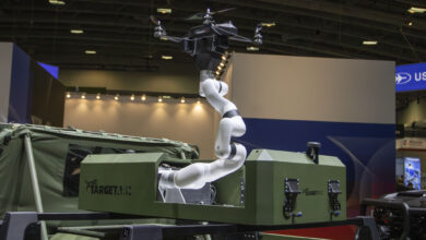 Robotic arm mounted on a military vehicle demonstrating its ability to launch and recover small drones in a defense technology exhibit