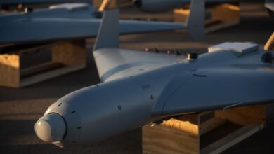 Close-up view of a LUCAS drone resting on a wooden stand, showing its sleek fixed-wing design and nose-mounted sensor under warm evening light.