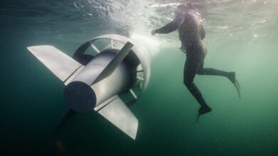 GreyShark AUV cruising underwater beside a diver, showing the autonomous vehicle’s streamlined design, rear fins, and propulsion system during subsea operations