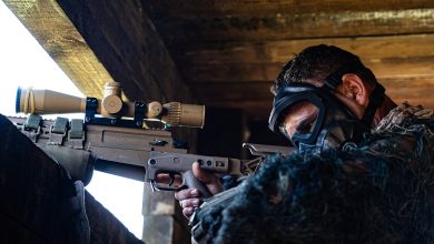Soldier wearing protective goggles aims a sniper from inside a concrete fighting position during a military training exercise.