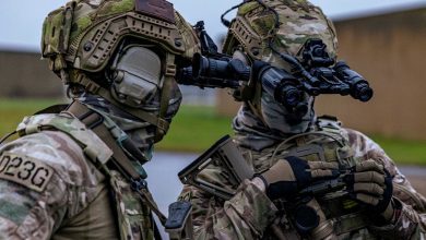 Two soldiers dressed in camouflage, observing with binoculars in a tactical setting.