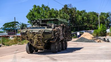 Royal Thai Navy amphibious 8x8 armored vehicle draped in camouflage netting and tire armor moving along a road during border defense operations