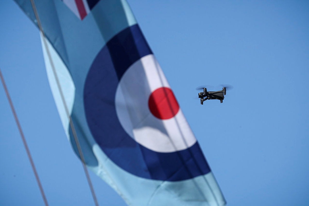 A compact quadcopter drone in flight alongside a Royal Air Force roundel banner during Exercise Agile Warrior, used to illustrate advances in quantum-resilient drone navigation and communications