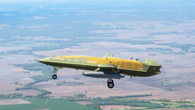 Boeing MQ-25A Stingray unmanned tanker aircraft in green primer and yellow livery during its historic first flight over a rural landscape for the U.S. Navy