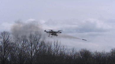 Serbian military autonomous quadcopter drone firing an aircraft rocket with a smoke plume trailing behind it over a bare winter treeline, showcasing the platform's multi-rocket air-to-ground strike capability