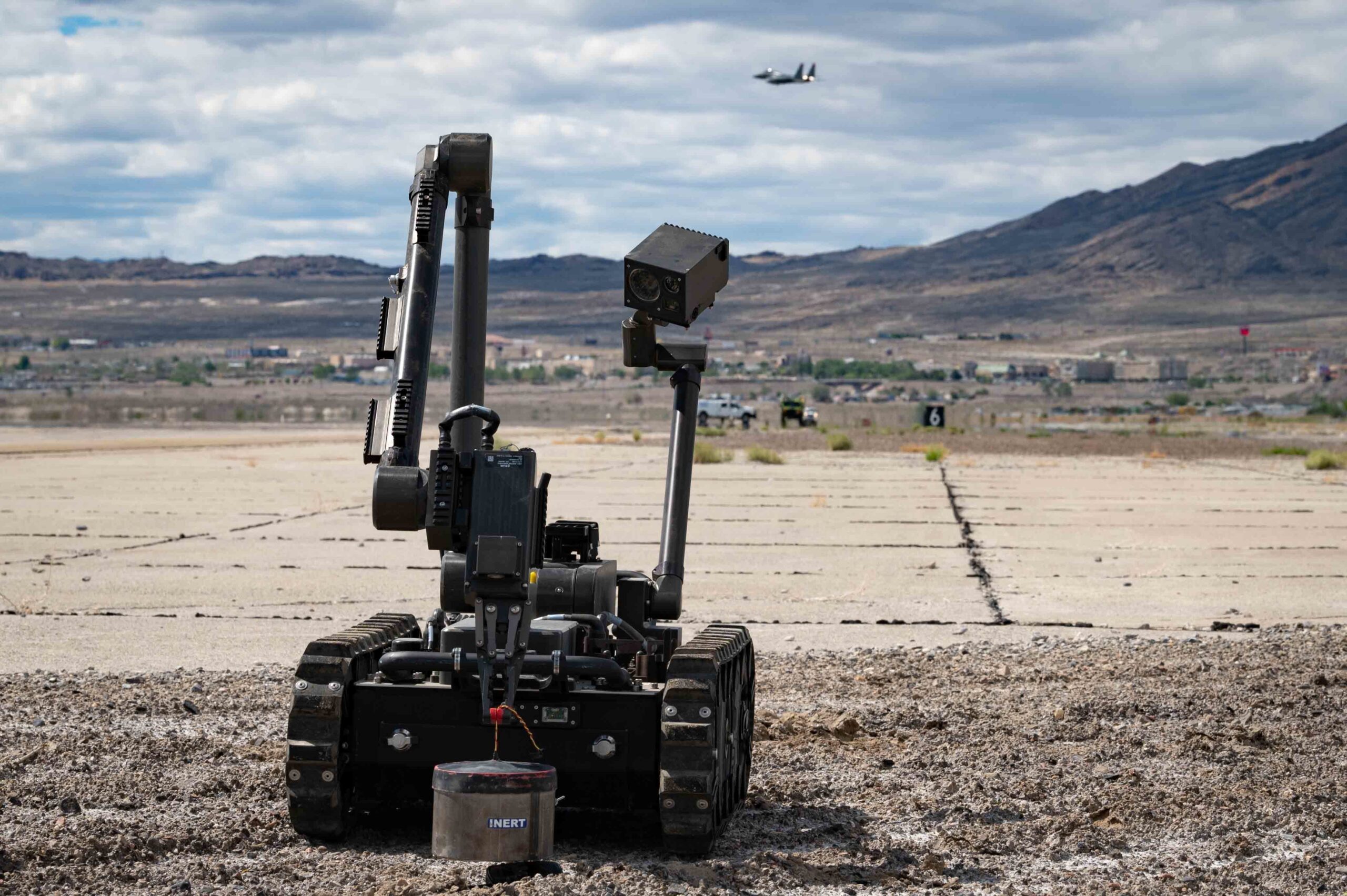 U.S. Air Force Airman 1st Class Garrett Haynie, 366th Civil Engineer Squadron explosive ordinance disposal technician, operates a bomb defusal robot while a 366th Fighter Wing F-15E Strike Eagle flies overhead at Wendover Air Field, Utah, May 20, 2022 as part of exercise Raging Gunfighter 22-2. This exercise prepares the 366th Fighter Wing for Agile Combat Employment (ACE) operations around the world. (U.S. Air Force photo by Staff Sgt. Danielle Charmichael)