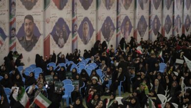 Crowd attending a memorial ceremony in Tehran beneath large portraits of civilians and military personnel killed in recent military operations.