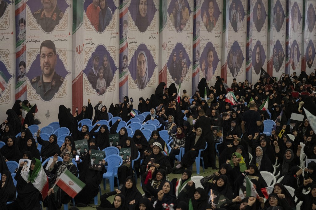 Crowd attending a memorial ceremony in Tehran beneath large portraits of civilians and military personnel killed in recent military operations.