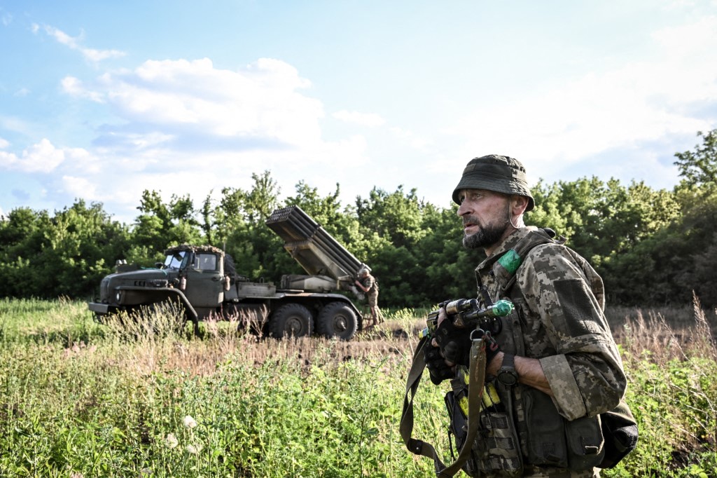 A soldier from the 148th Separate Artillery Zhytomyr Brigade of the Ukrainian Airborne Forces stands guard as servicemen prepare to fire missiles from a BM-21 Grad multiple launch rocket system at Russian positions in the Oleksandrivka sector, Dnipropetrovsk region, Ukraine, on June 22, 2026. (Photo by Dmytro Smolienko/Ukrinform/NurPhoto via AFP)
